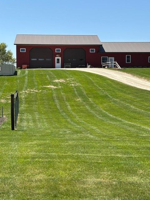 Red barn with white roof beside a grassy sloped driveway under a clear blue sky