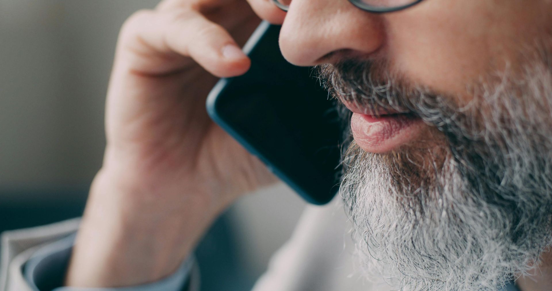 Close-up of a bearded man speaking on a smartphone, wearing glasses