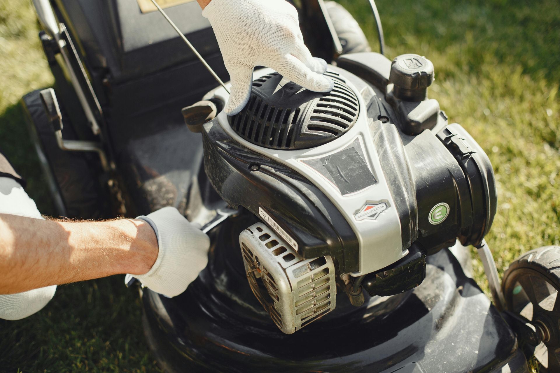 Gloved hands adjusting a lawn mower engine in sunlight