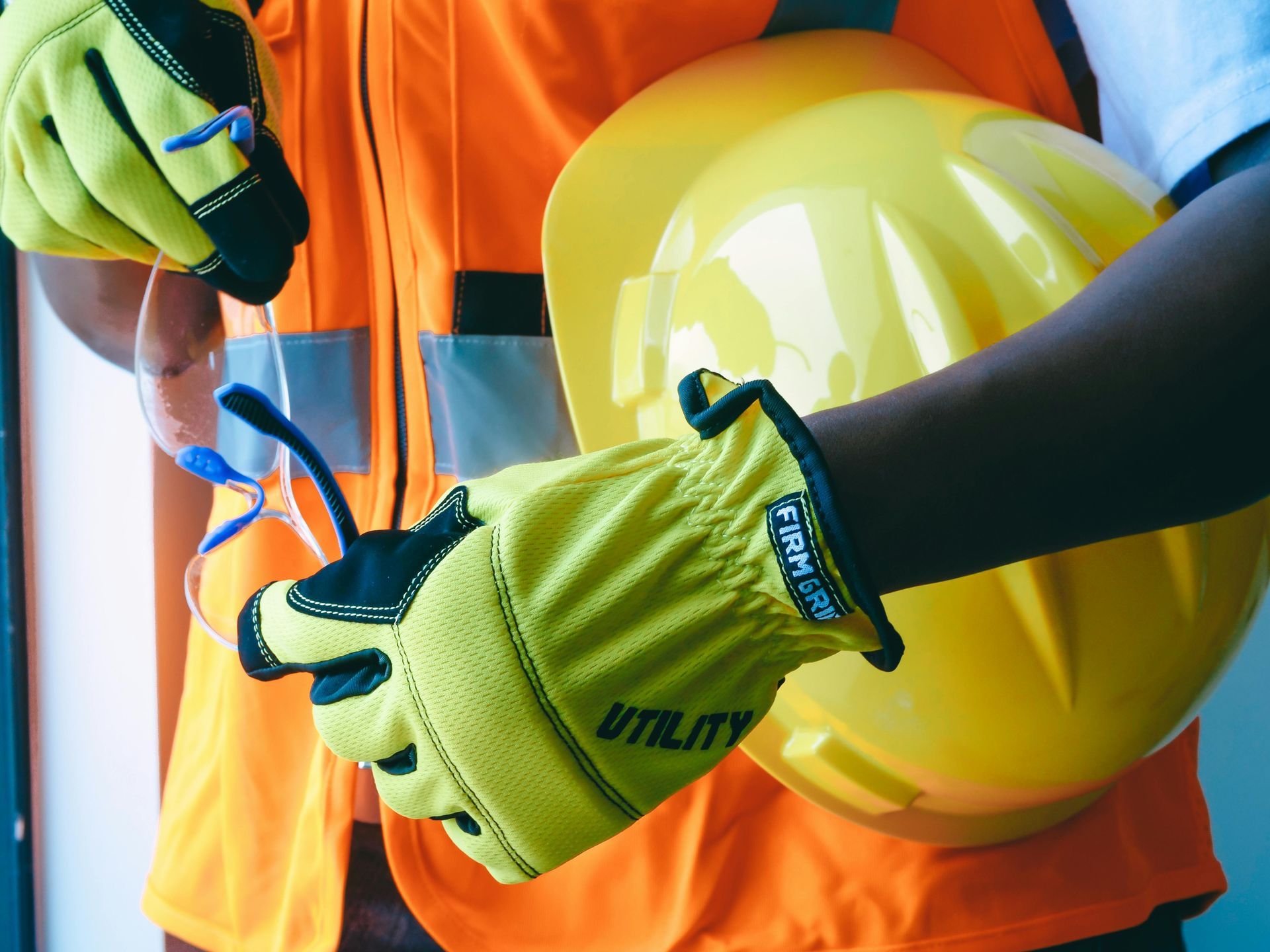 Workers in safety vests and gloves handling tools with a yellow hard hat nearby