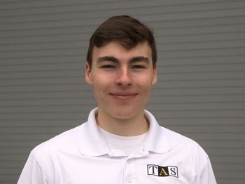 A young man wearing a white polo shirt is smiling for the camera.