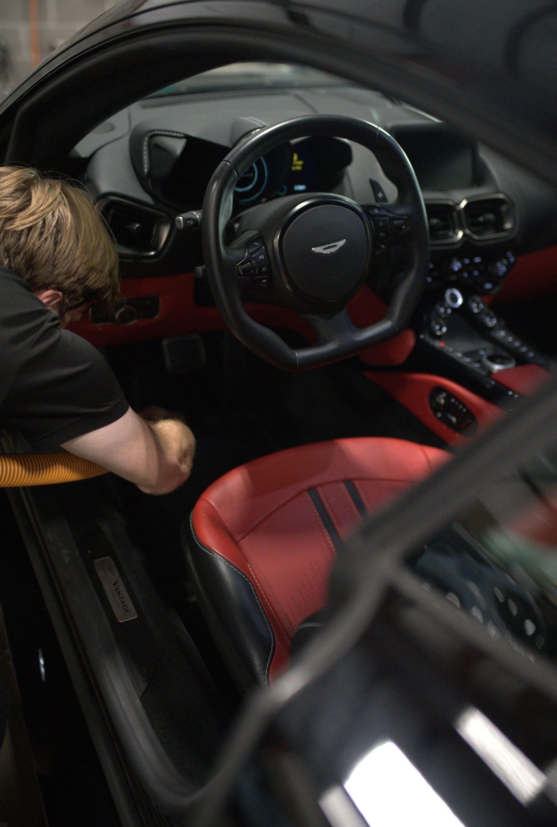 Person cleaning the red and black interior of a black Aston Martin.