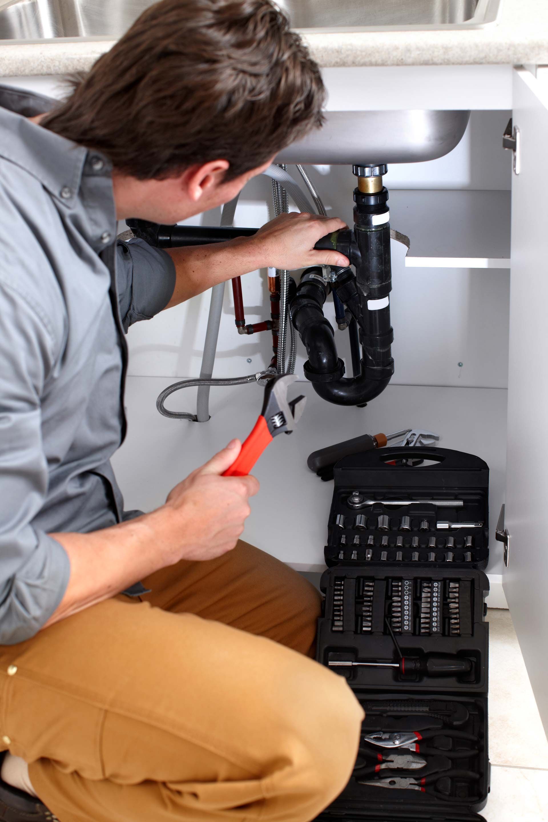 A plumber works under a kitchen sink