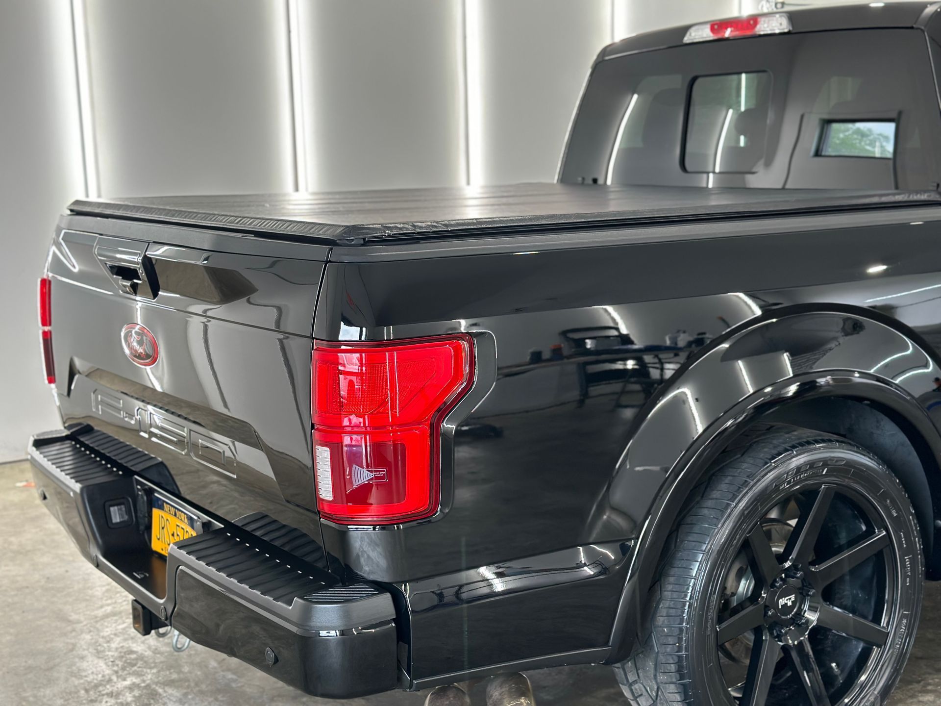 A black Ford F-150 truck with a tonneau cover and custom black wheels parked in a garage.