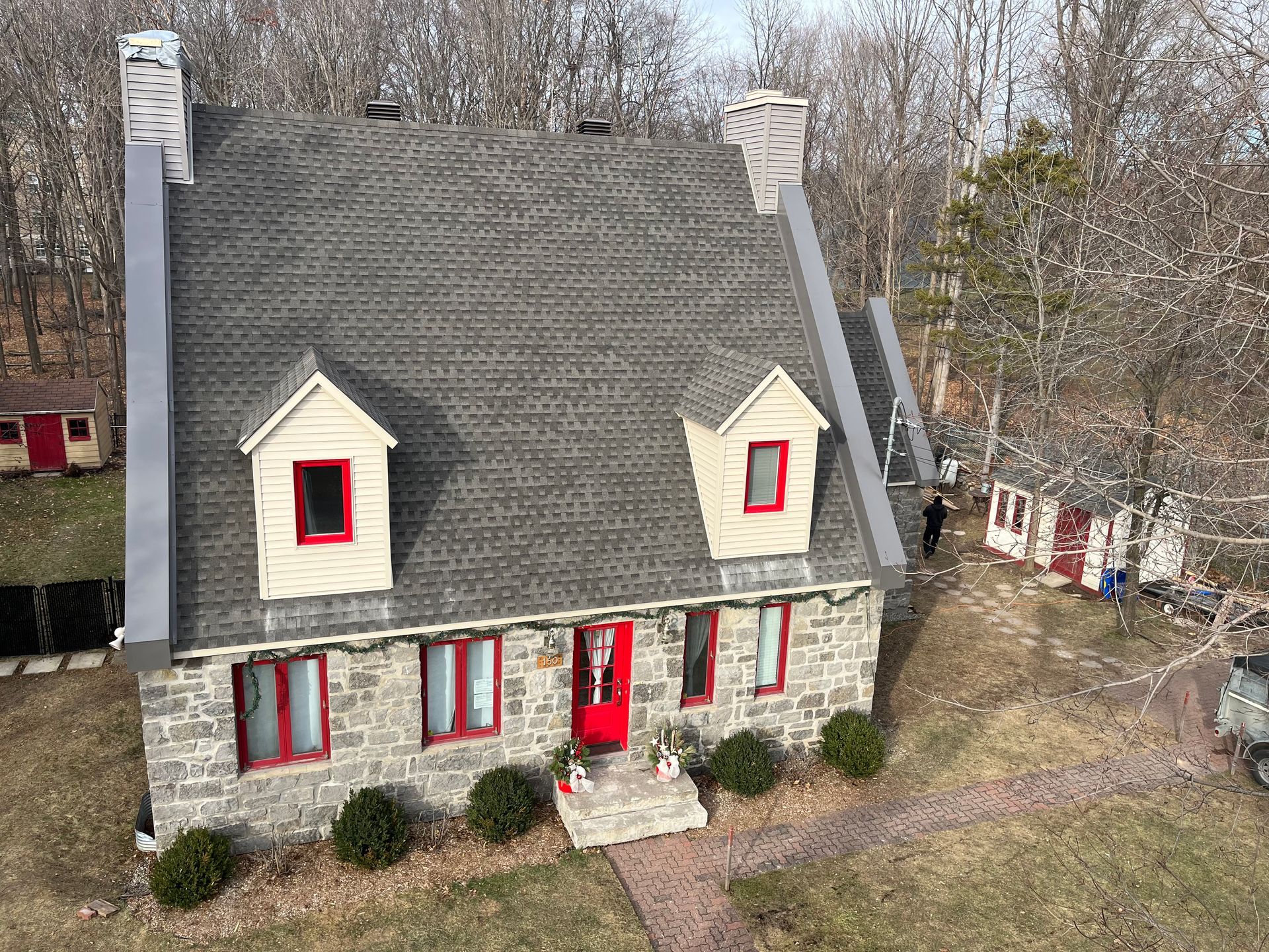 Une vue aérienne d'une maison en pierre avec des fenêtres rouges et un toit gris.