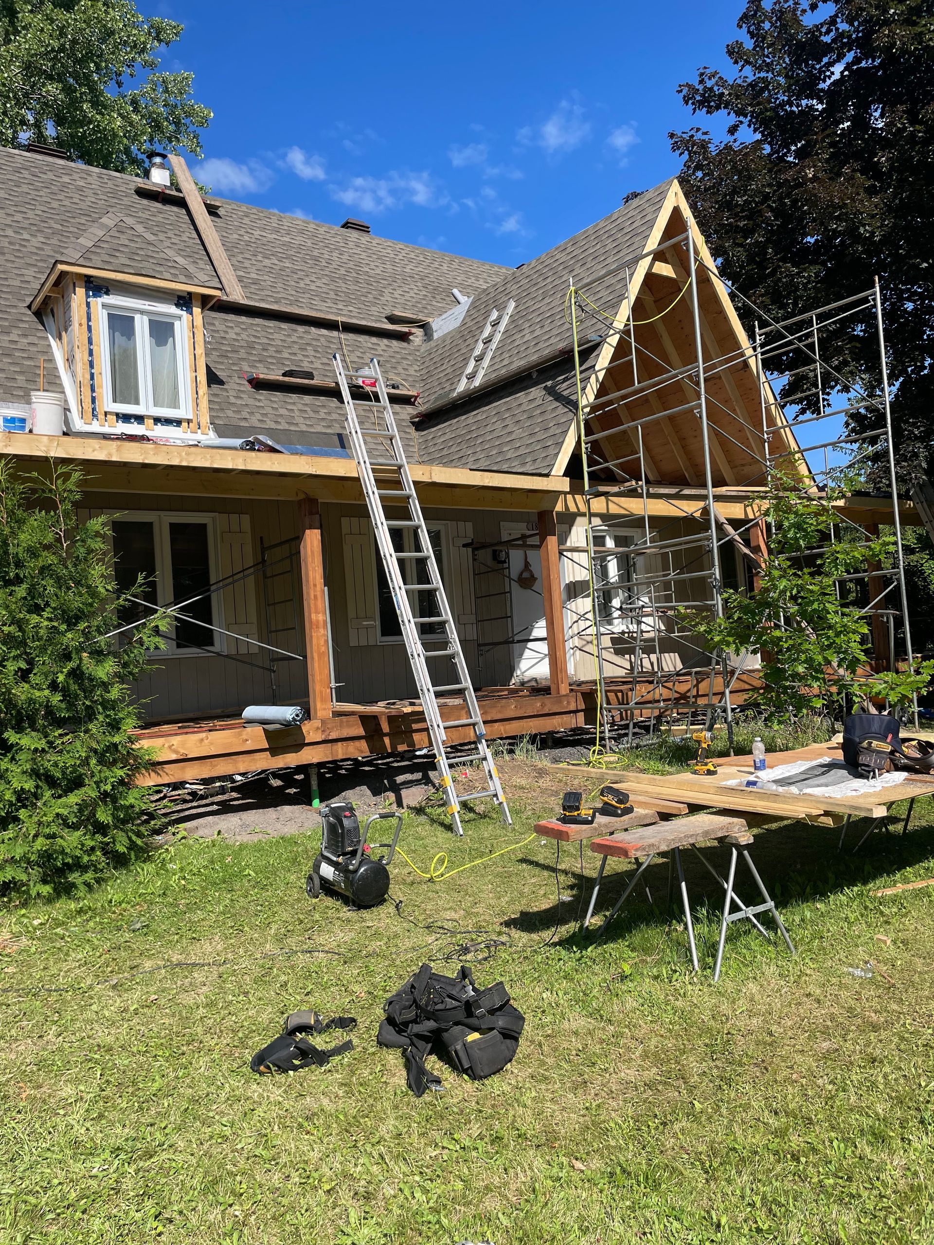 Maison en rénovation avec échafaudage, échelle et outils dans une cour par une journée ensoleillée.