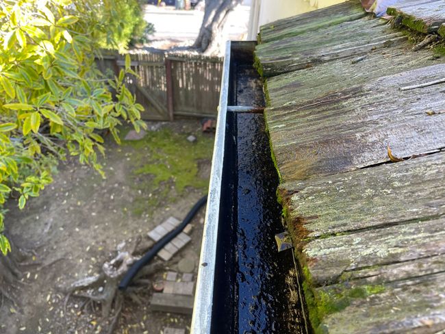 A black gutter is sitting on top of a wooden roof.