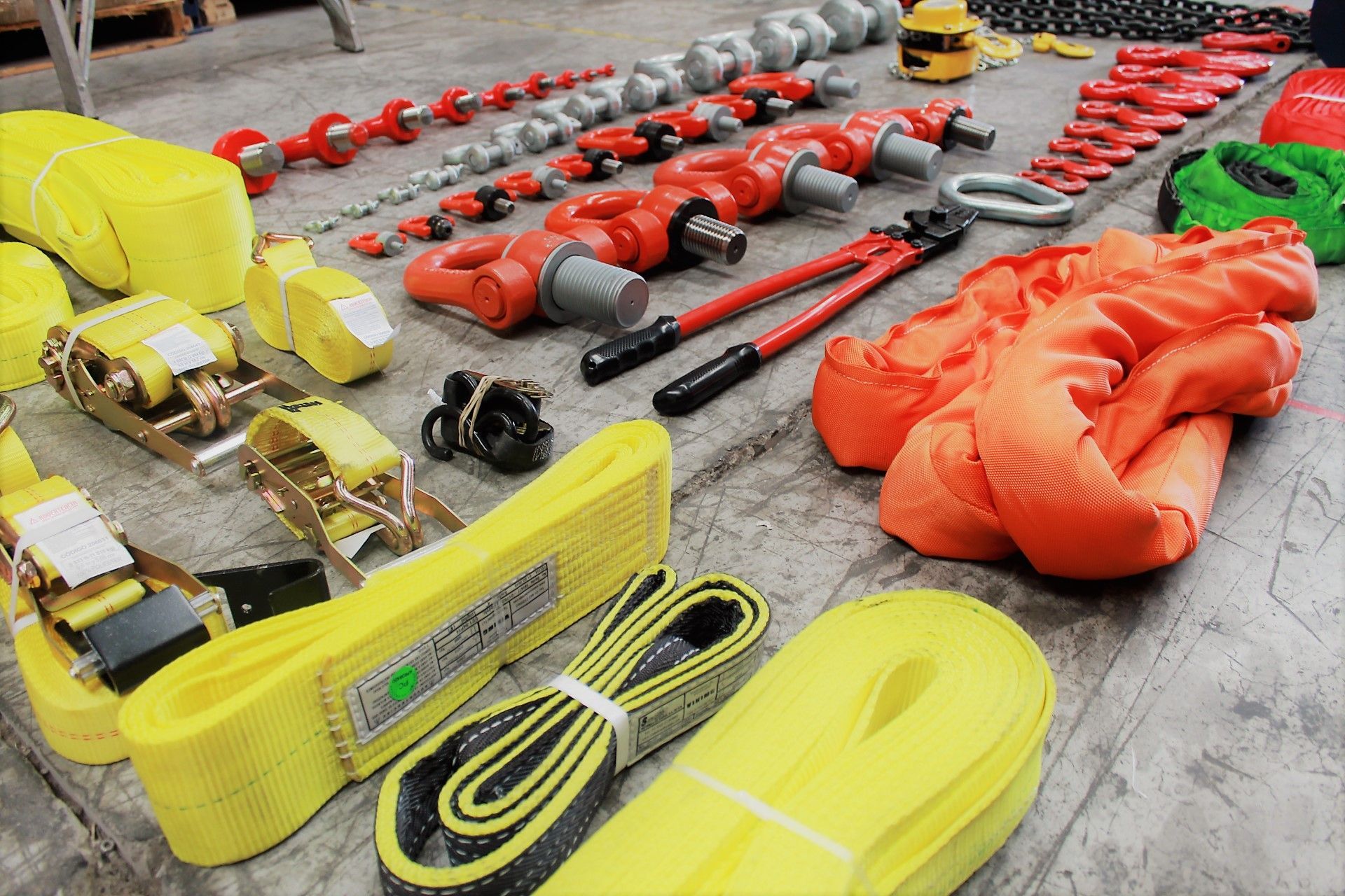 Equipos variados de aparejo y elevación: eslingas, grilletes, cadenas, cortadores y otras herramientas industriales, sobre un piso de concreto.