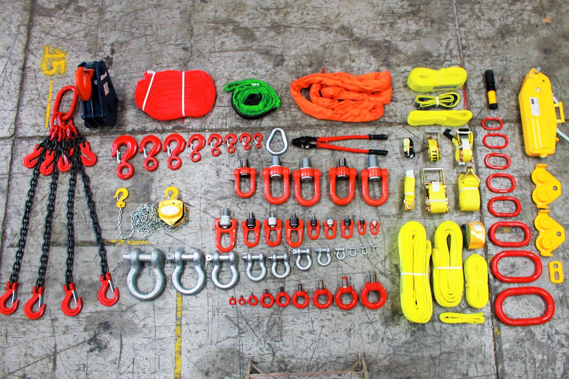 Diversos equipos de elevación y aparejo dispuestos sobre una superficie de hormigón, incluidas cadenas, ganchos y eslingas.