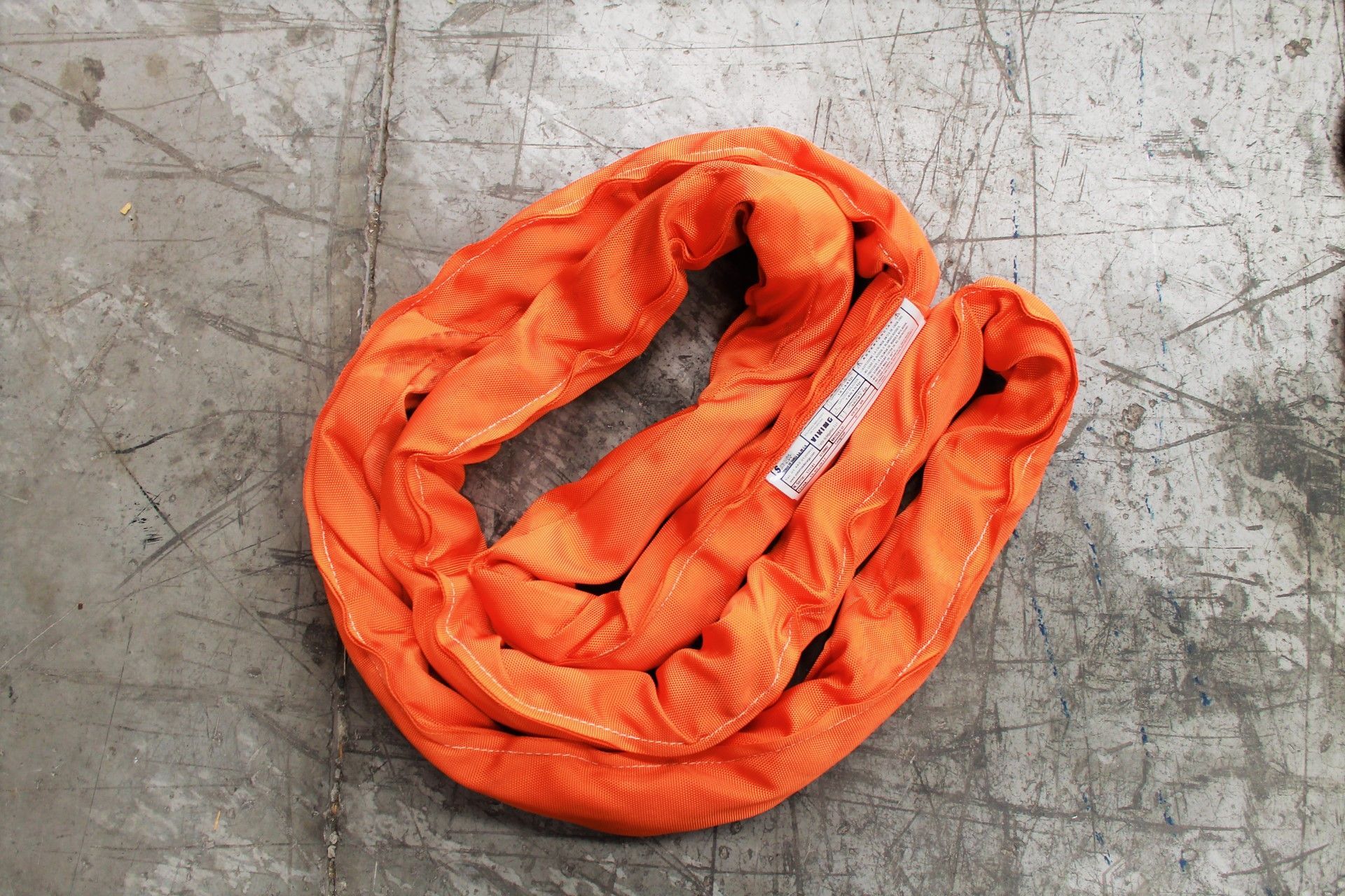 Eslinga de elevación de color naranja enrollada sobre una superficie de hormigón.