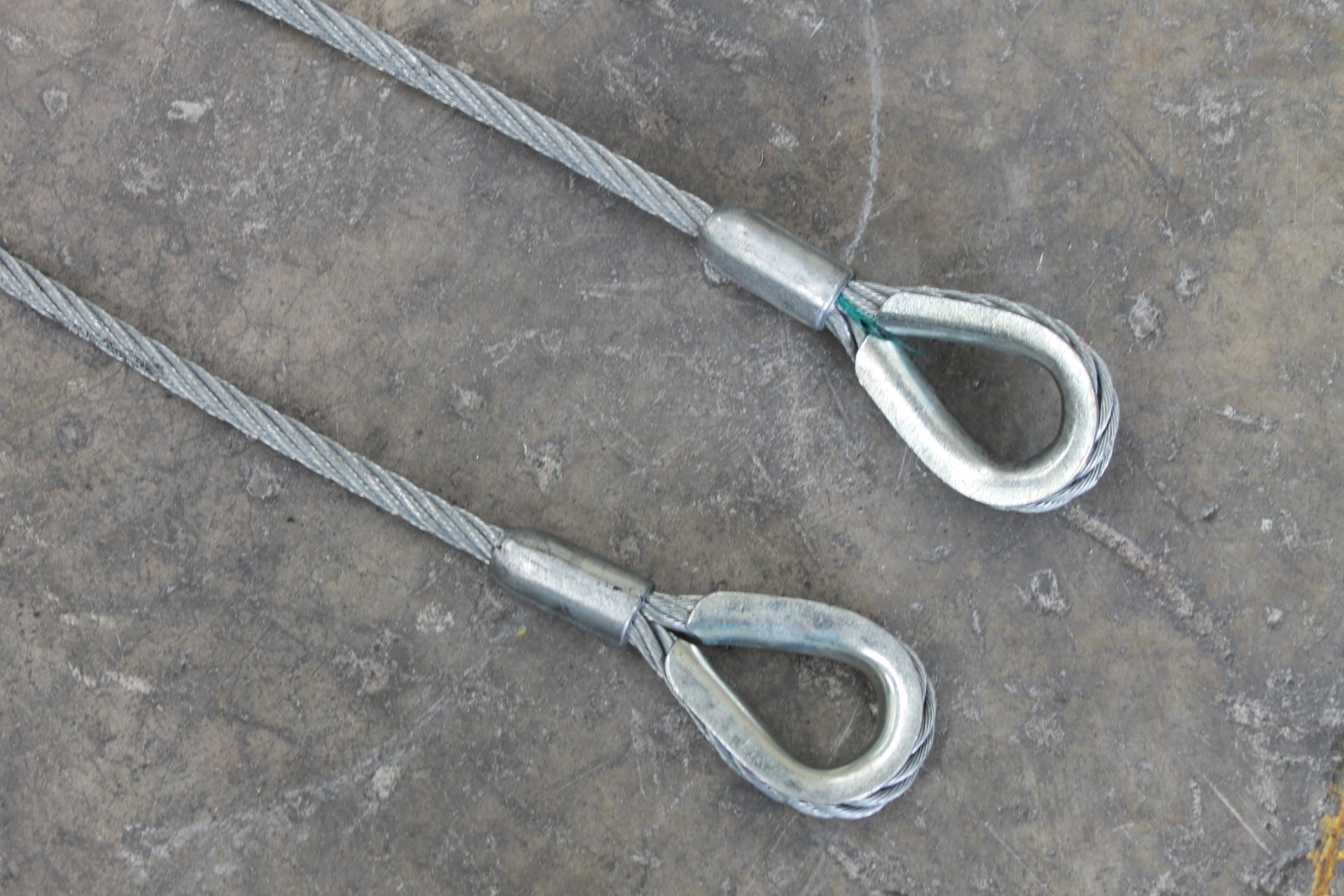 Dos bucles de cable de acero con guardacabos metálicos, colocados sobre una superficie gris.