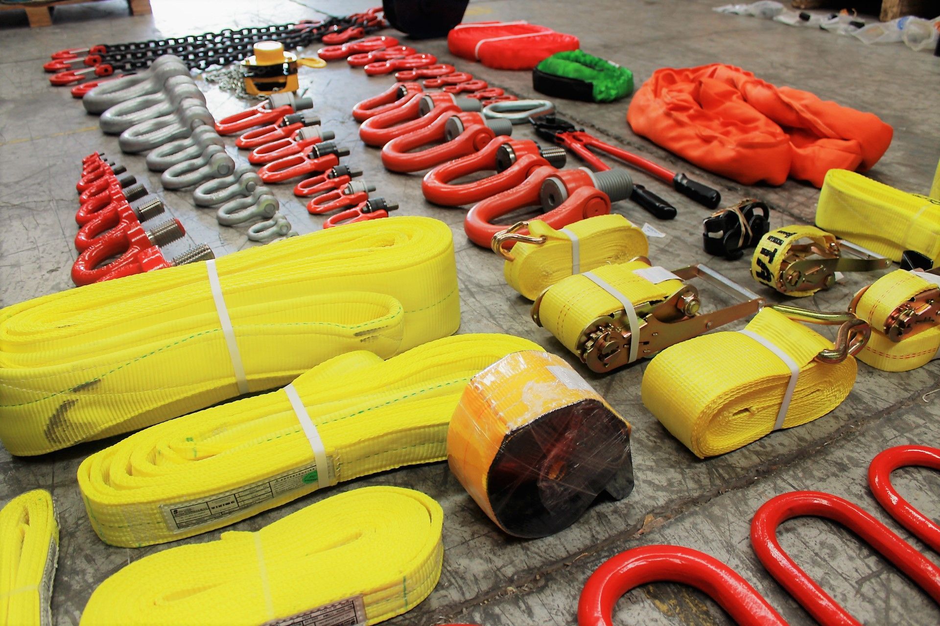 Surtido de equipos de aparejo, incluidas cadenas, correas y ganchos, dispuestos sobre un piso de concreto.