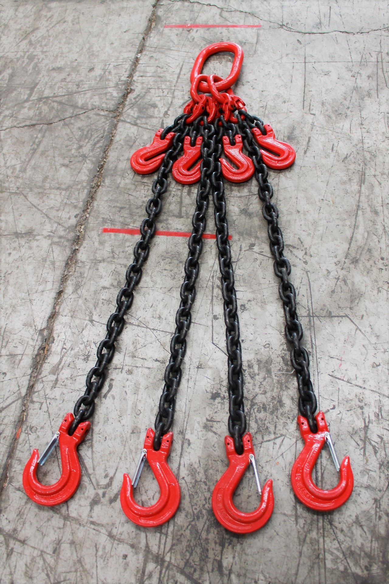 Cadena de elevación de cuatro patas de color rojo y negro con un anillo superior y cuatro ganchos, colocada sobre una superficie de hormigón.