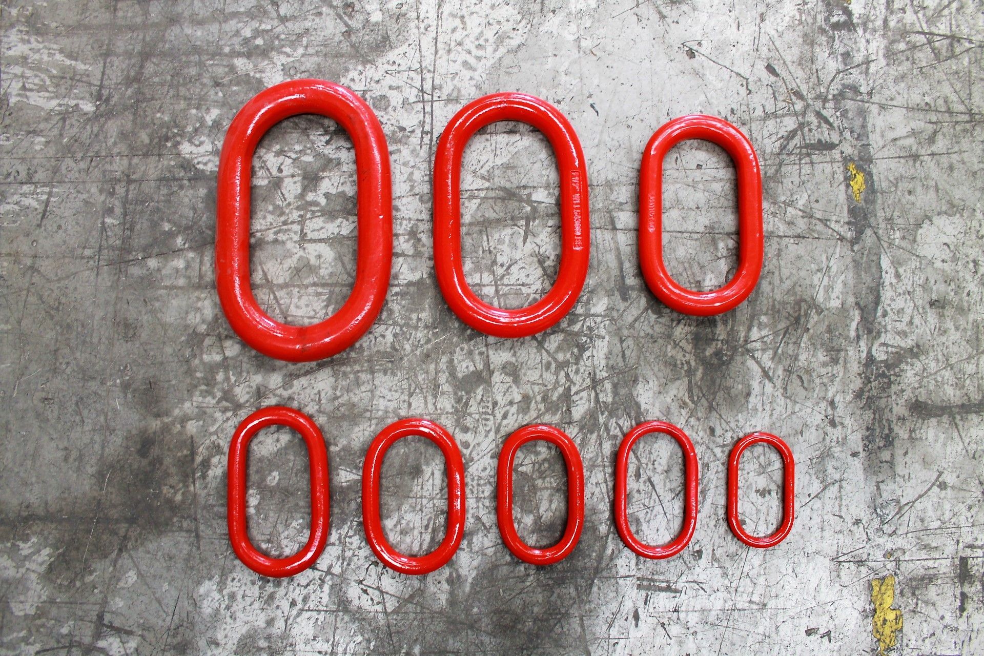 Siete eslabones metálicos rojos, ovalados y de distintos tamaños, dispuestos sobre una superficie gris texturizada.