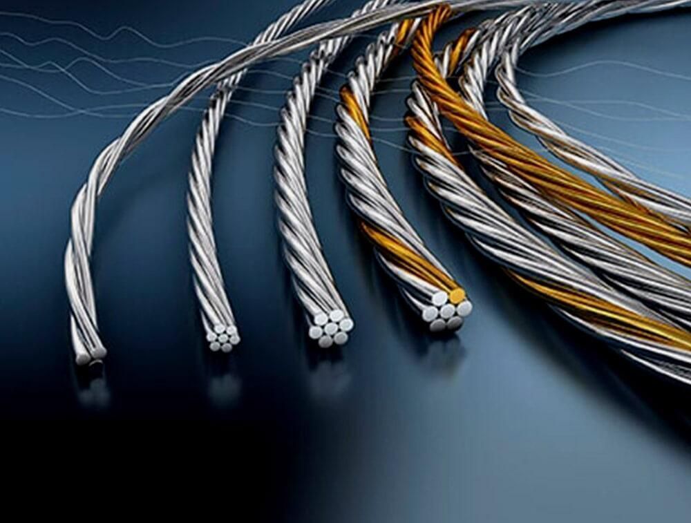 Surtido de cables de acero de distintos espesores, algunos con núcleos de color dorado, sobre un fondo degradado azul oscuro.