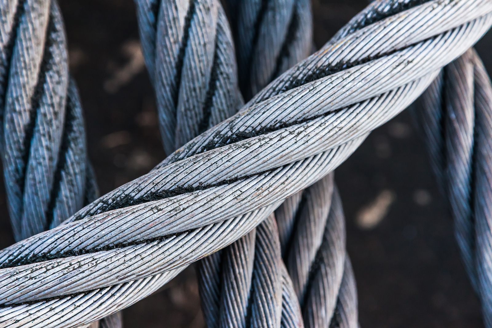 Primer plano de tres cables de acero gruesos y retorcidos, de color gris y texturizados sobre un fondo oscuro.