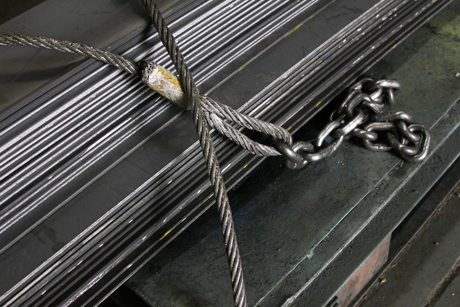 Cables de acero y cadena que aseguran una pila de láminas de metal.