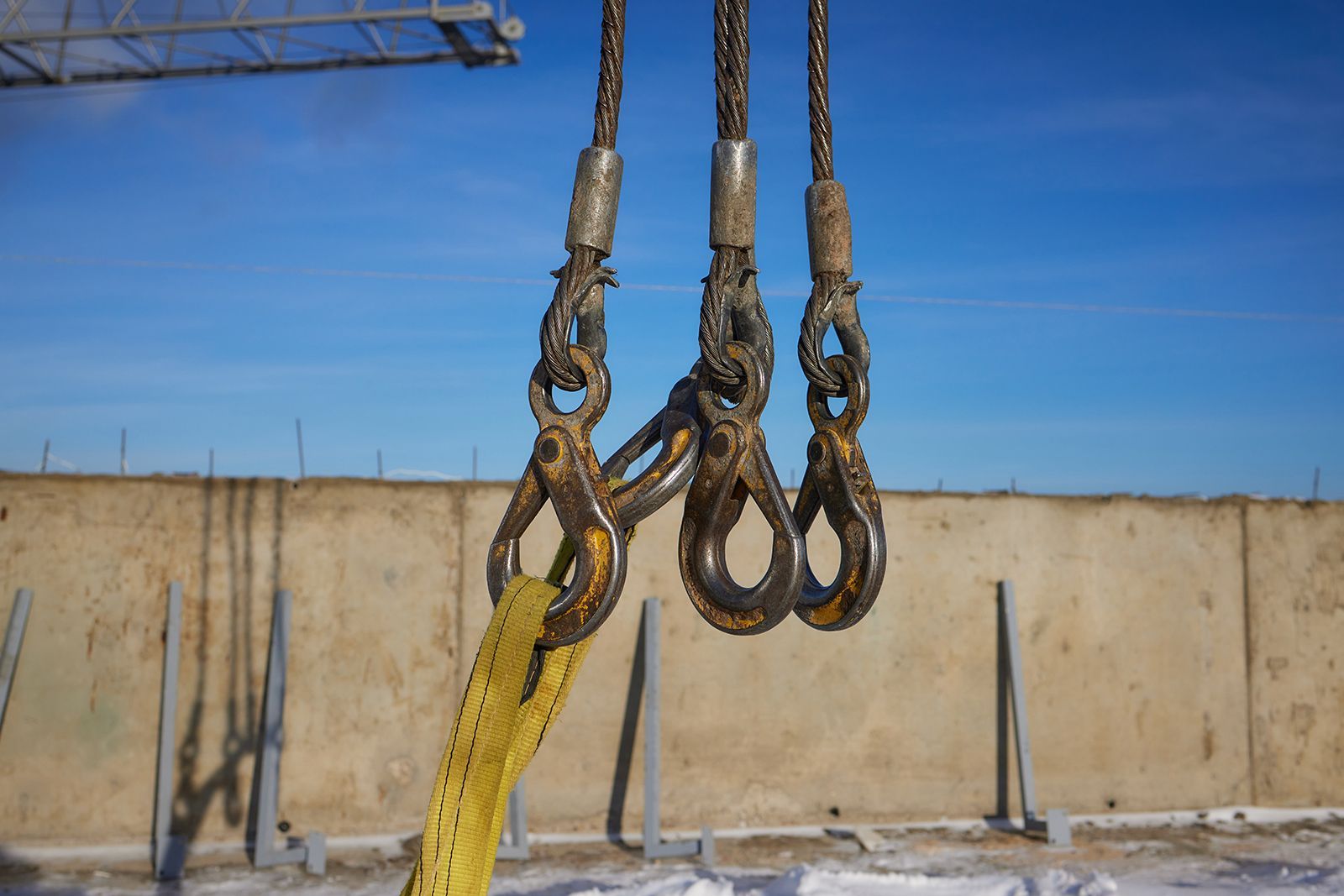 Tres cables de acero con ganchos que suspenden una correa amarilla; al aire libre.