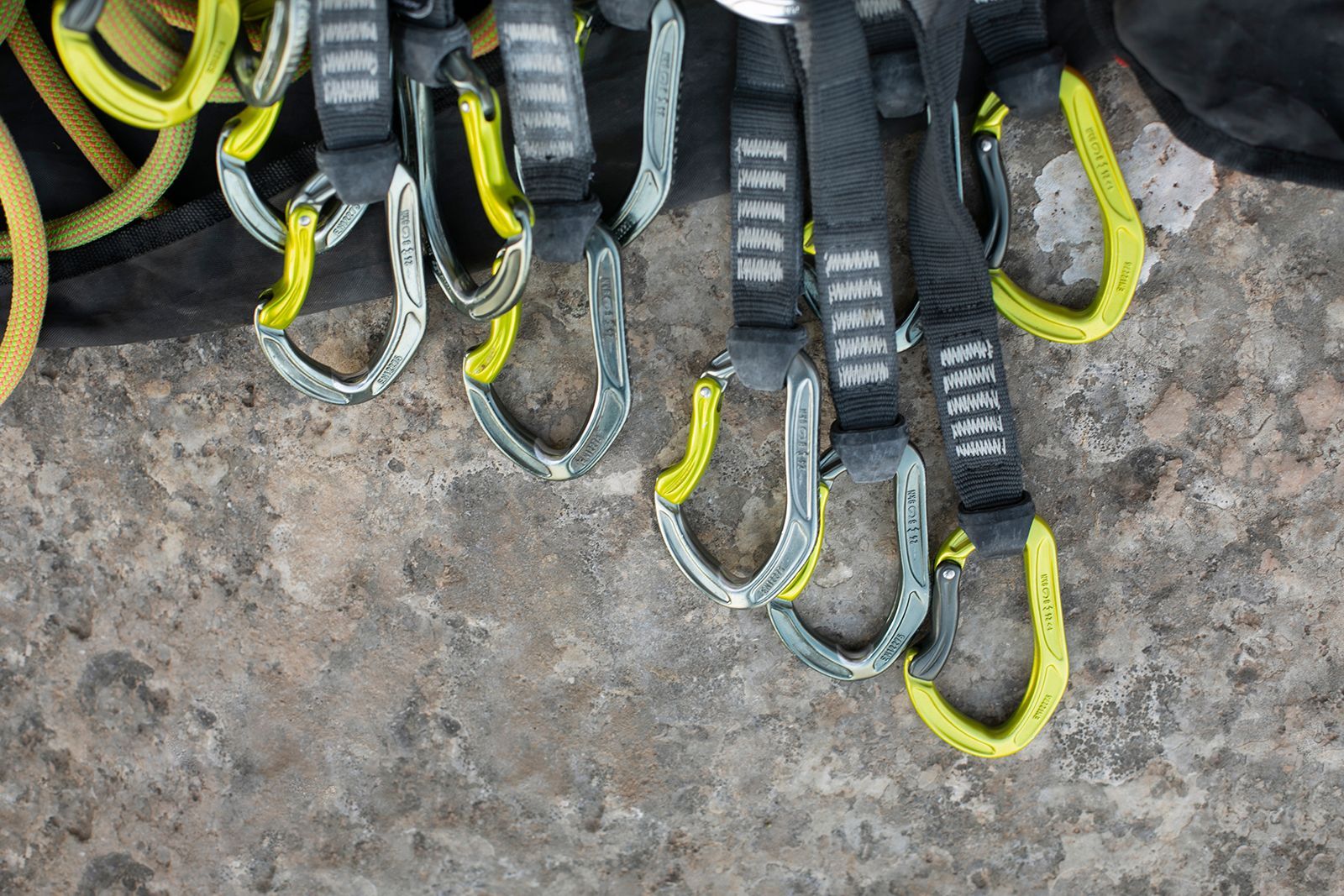 Equipo de escalada en roca: mosquetones con detalles amarillos colgados sobre una superficie de hormigón.