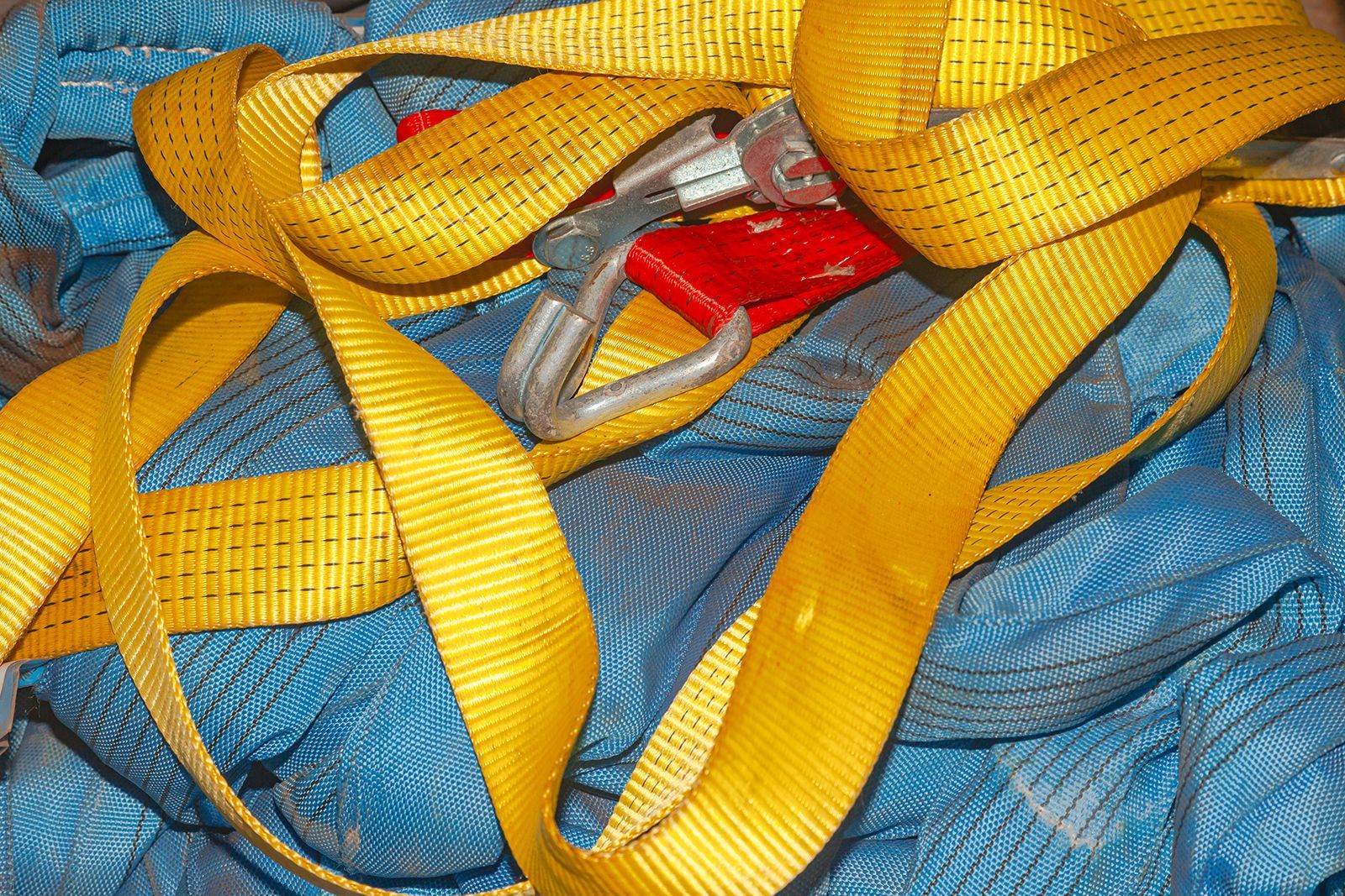 Correas de amarre de color amarillo con un gancho rojo y plateado, que descansan sobre un material de malla azul.