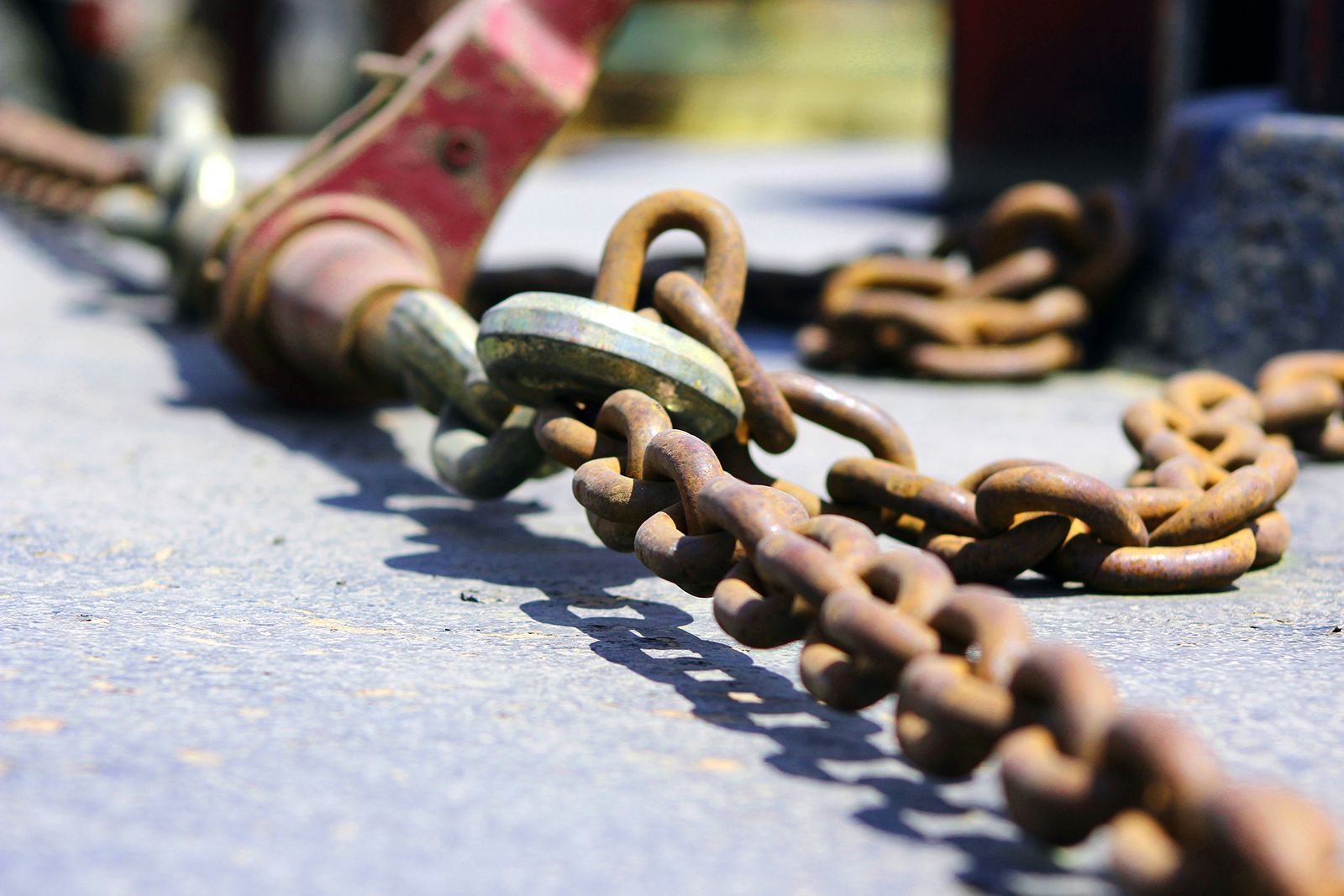 Cadena oxidada unida a un polipasto rojo sobre una superficie de hormigón.
