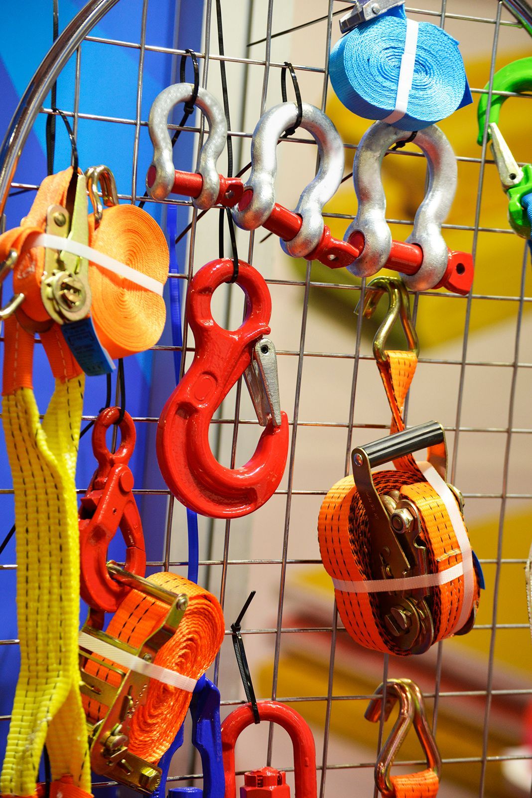 Surtido de correas de amarre y ganchos industriales coloridos exhibidos sobre una rejilla de alambre.