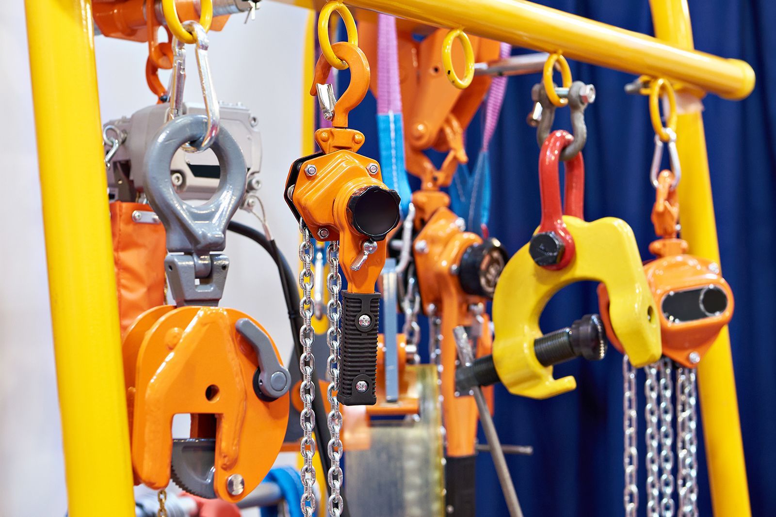 Varias herramientas de elevación y aparejo industriales, en su mayoría de color naranja, colgadas de un soporte amarillo.