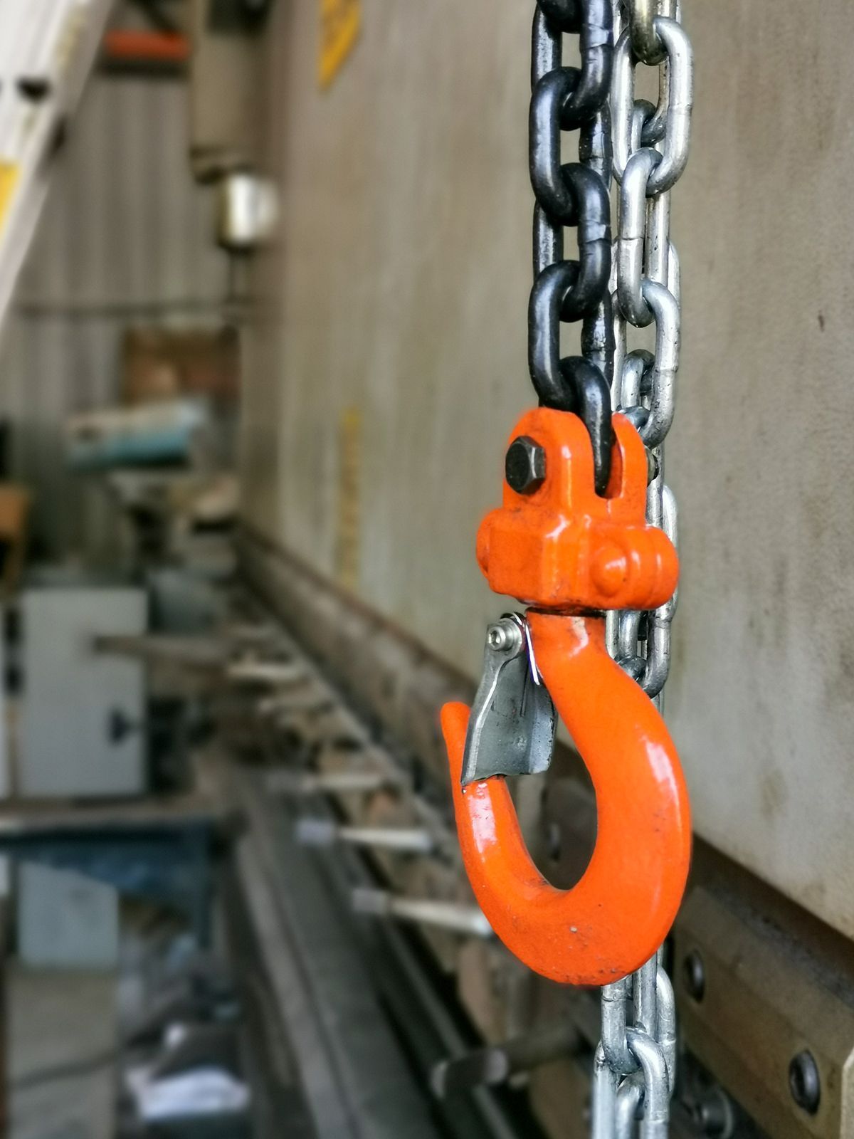 Gancho naranja unido a una cadena que cuelga en un entorno de taller.