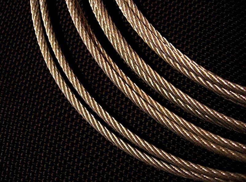 Primer plano de varios hilos de cable de acero retorcidos sobre un fondo negro texturizado.