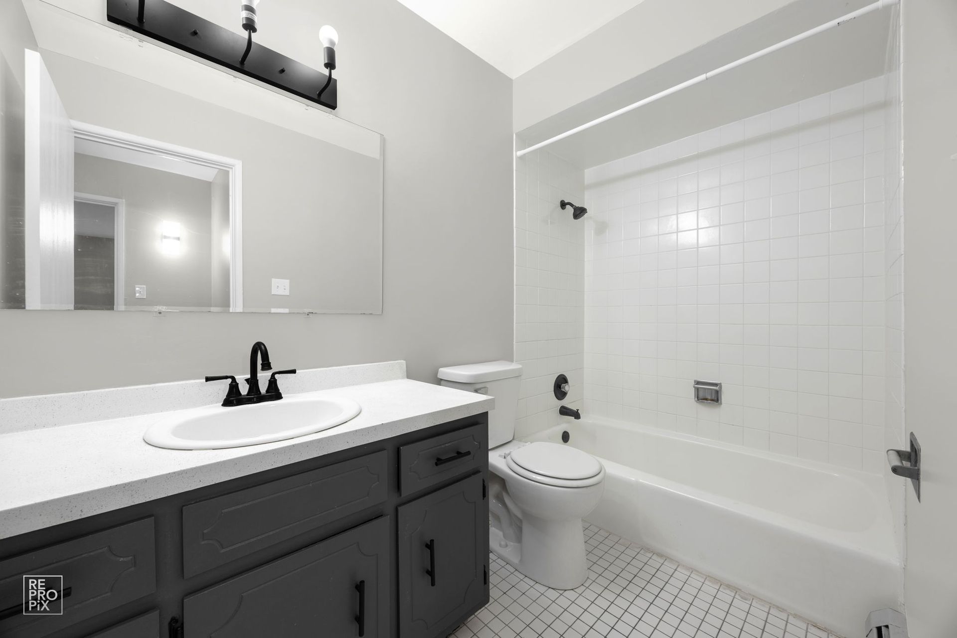 Gray and white bathroom with vanity, toilet, and shower/tub combo.