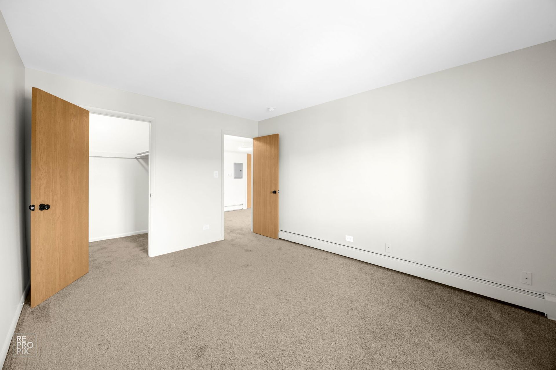 Empty bedroom with beige carpet, light gray walls, and brown doors.