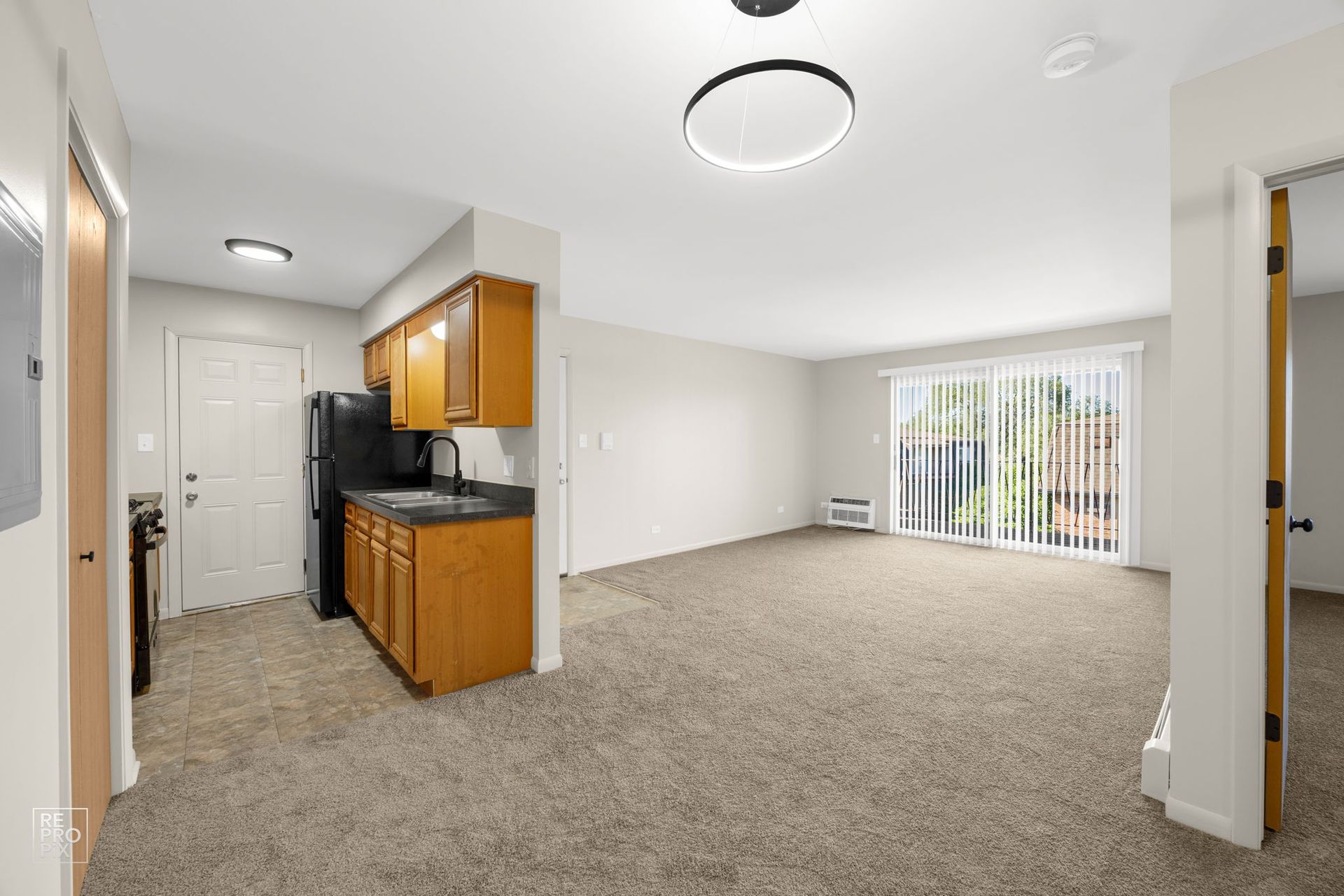 An empty apartment interior with kitchen, living area, and sliding glass doors. Brown carpet and cabinets.