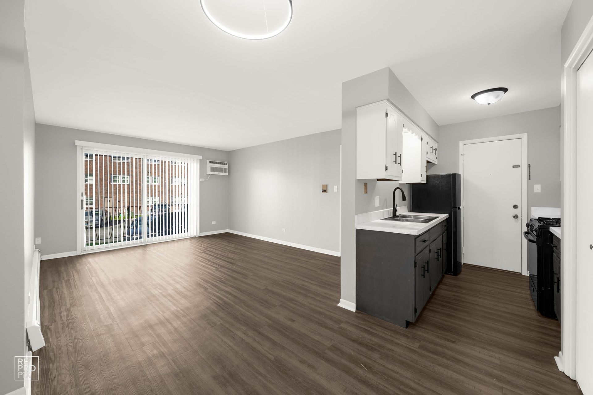 Empty apartment interior with a kitchen, sliding door, and wood flooring.