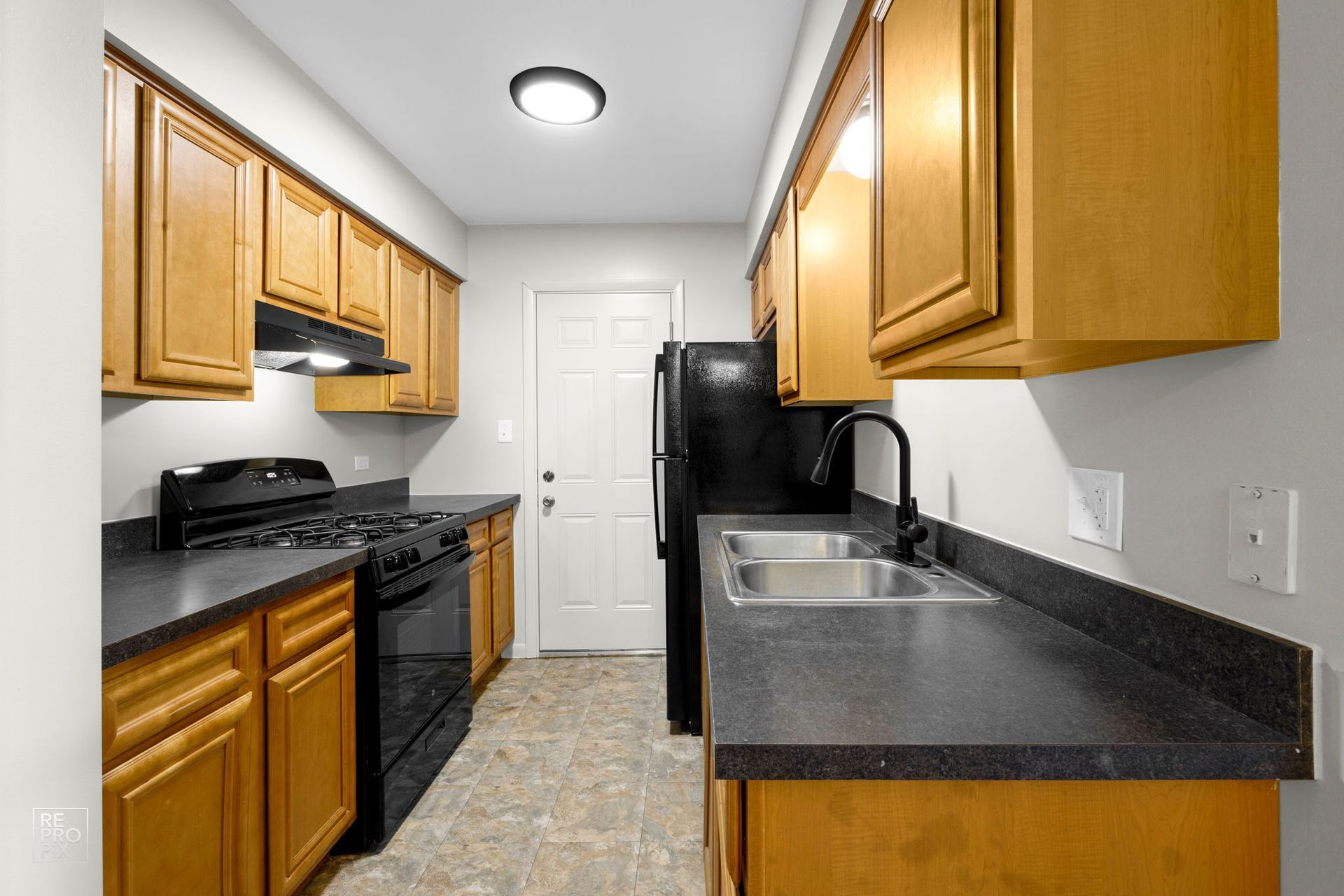 Kitchen with wooden cabinets, black appliances, grey countertops, and a door.