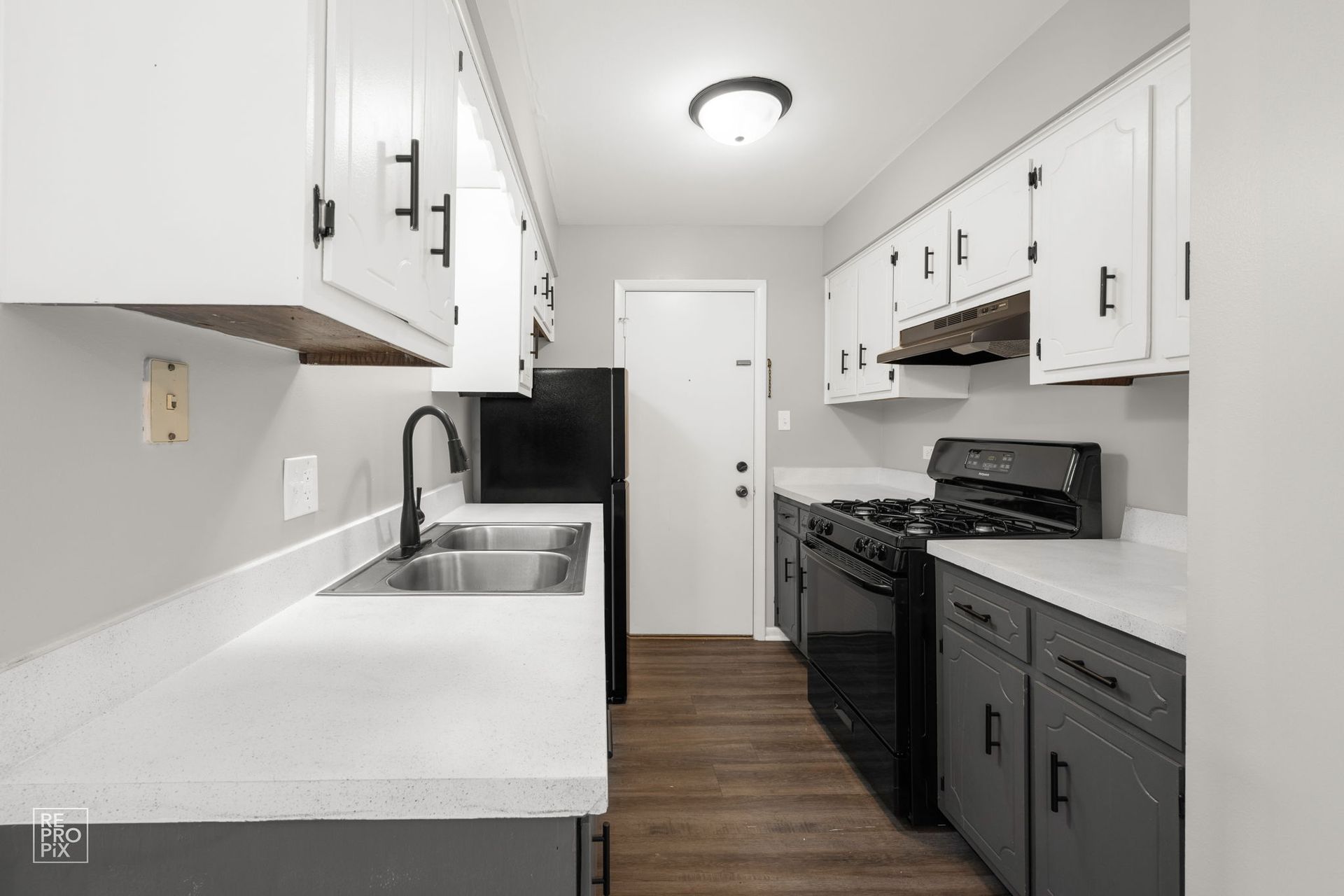 Narrow kitchen with white cabinets, gray lower cabinets, black appliances.