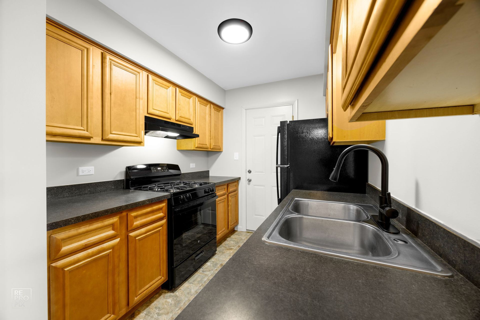 Small kitchen with light wood cabinets, black appliances, and a stainless steel sink.
