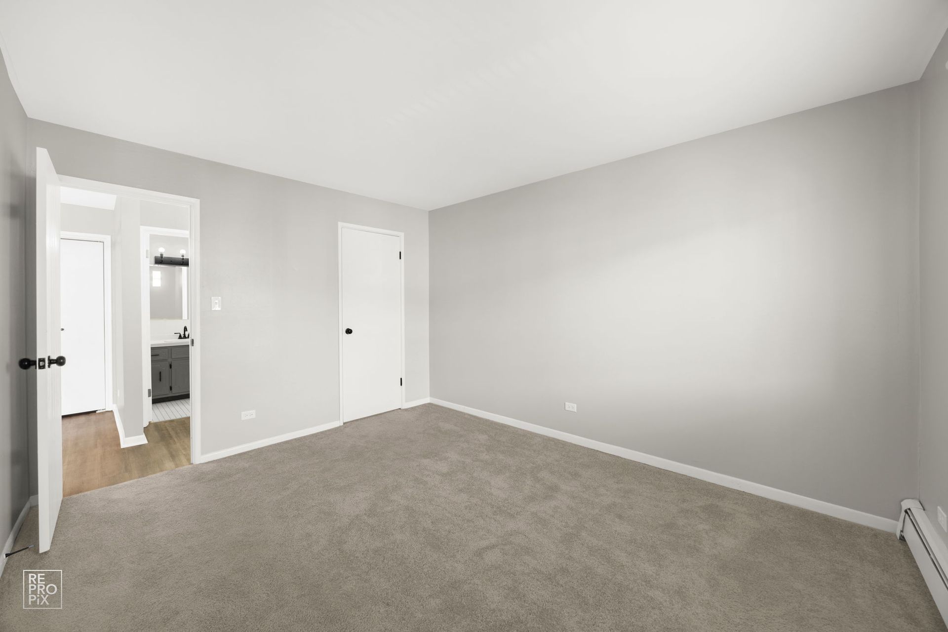 Empty bedroom with gray walls and carpet, two doorways, and a radiator.