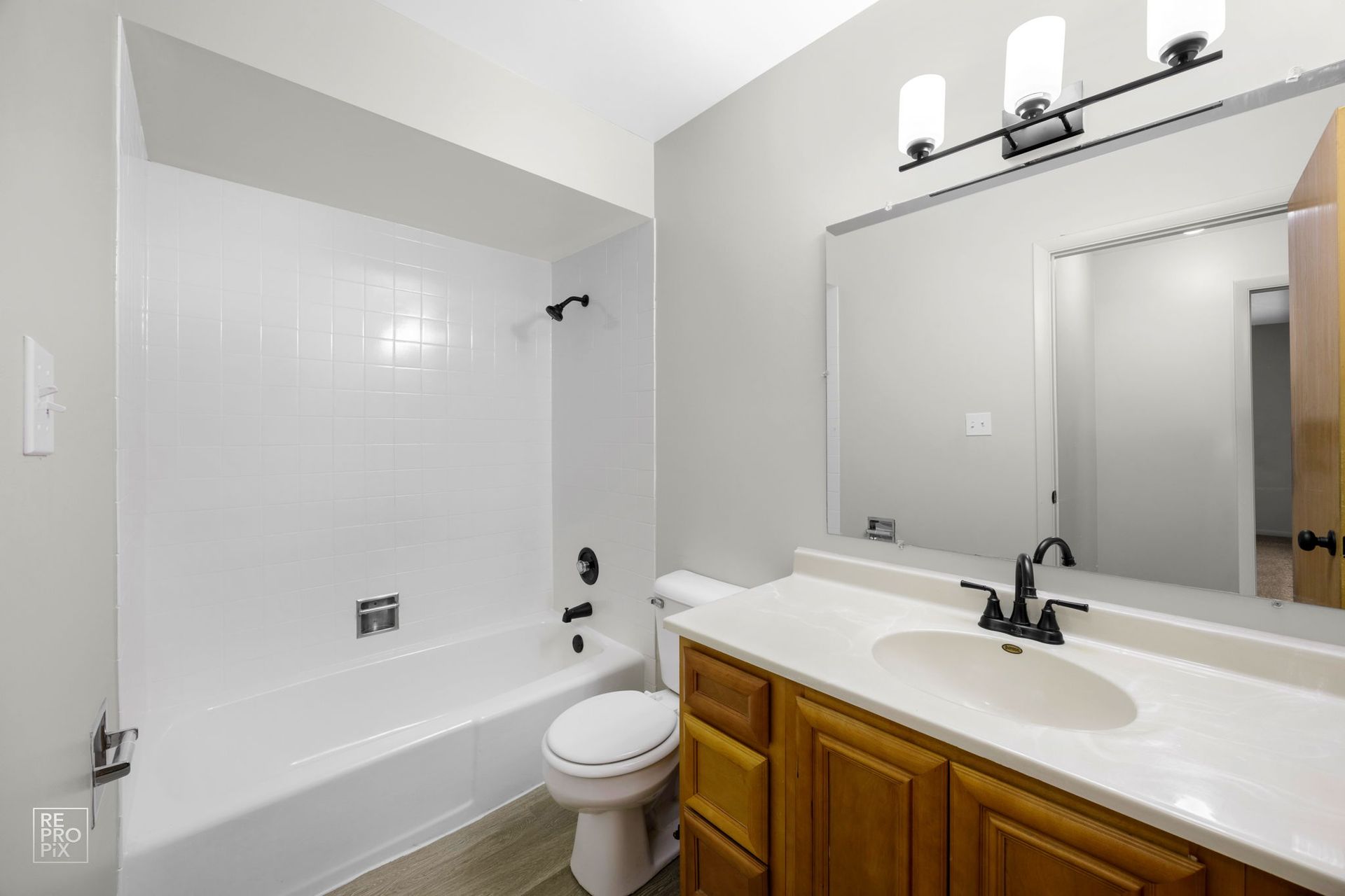 Bathroom with white tub, toilet, light wood vanity, large mirror, and black fixtures.