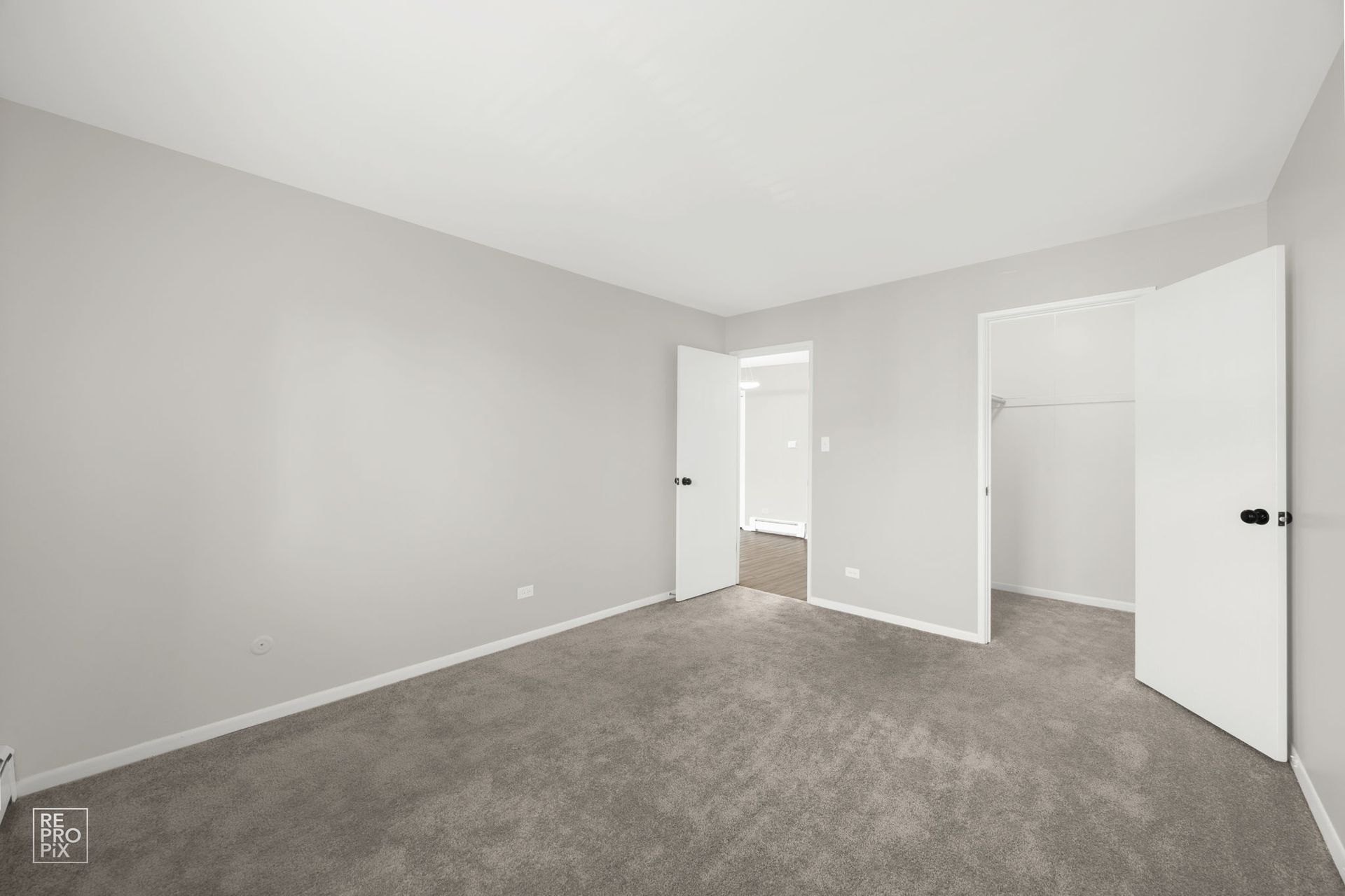 Empty bedroom with gray carpet, light gray walls, and white doors leading to a closet and bathroom.