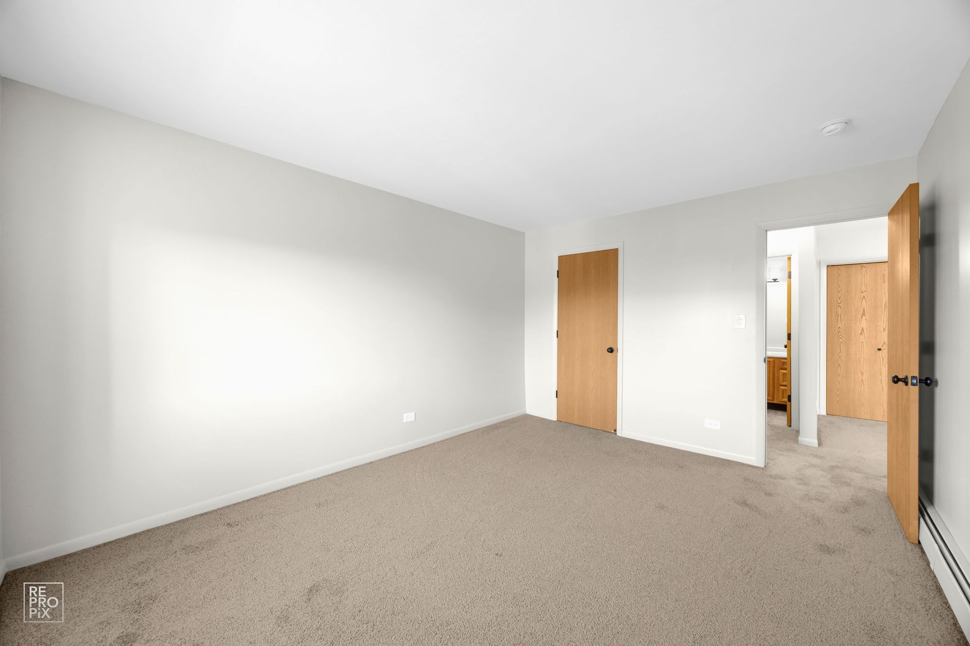Empty bedroom with light tan carpet, beige walls, and wood doors.