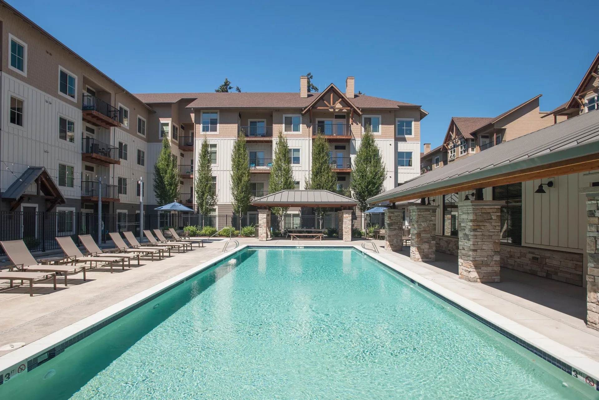 Outdoor pool area at an apartment community with lounge chairs and surrounding buildings.