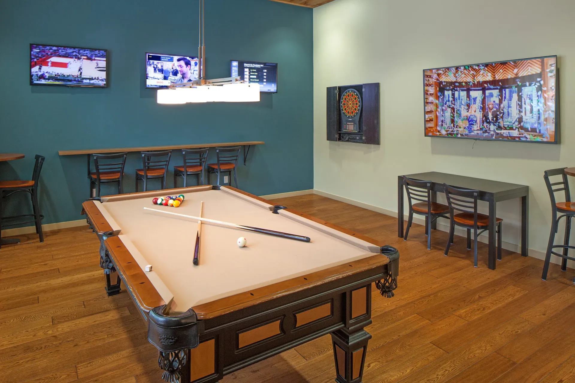 Indoor community game room with a pool table, bar-height seating, and wall-mounted TVs.