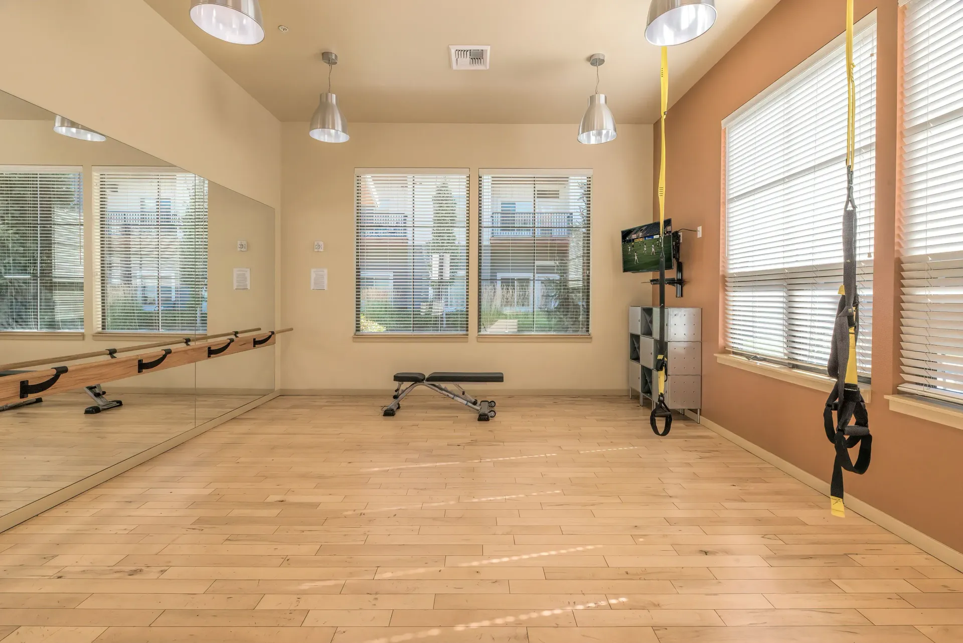 Fitness studio in a residential community with mirrors, wooden floor, TRX straps, and a small bench.