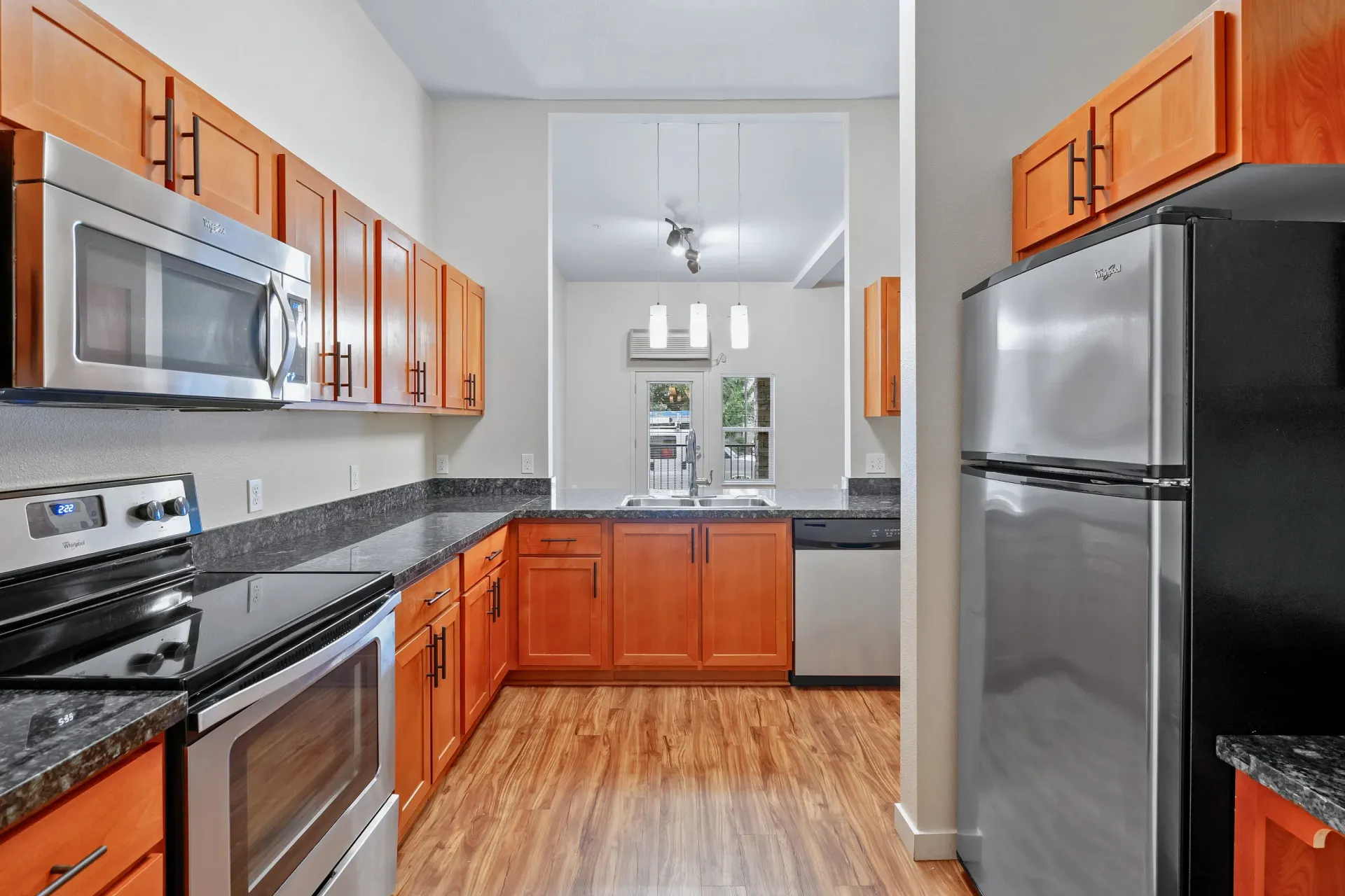 Modern apartment kitchen with wood cabinets, stainless steel appliances, and a double sink.