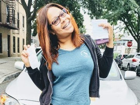 A woman is standing in front of a car holding a wallet.