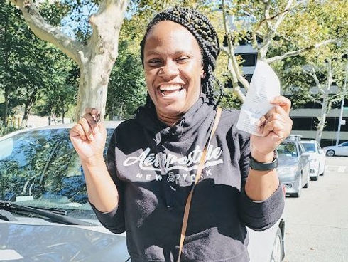 A woman is holding a piece of paper in front of a car.
