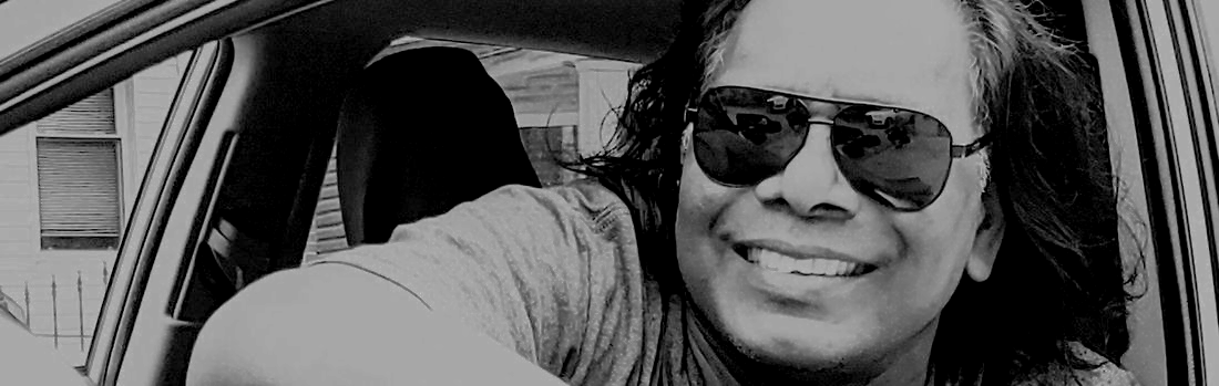 A man wearing sunglasses is sitting in a car and smiling.