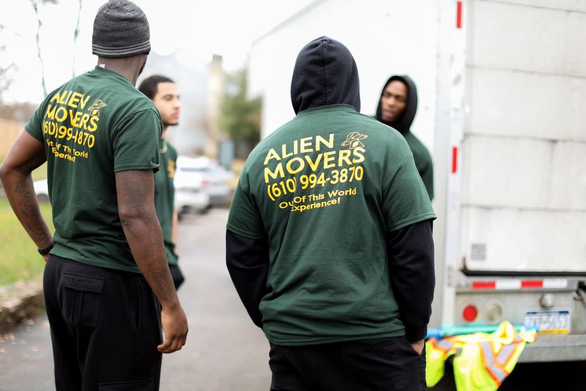 A punctual team of Alien Movers, dressed in branded green apparel, stands ready near their truck, exemplifying timely and reliable moving services in Philadelphia.