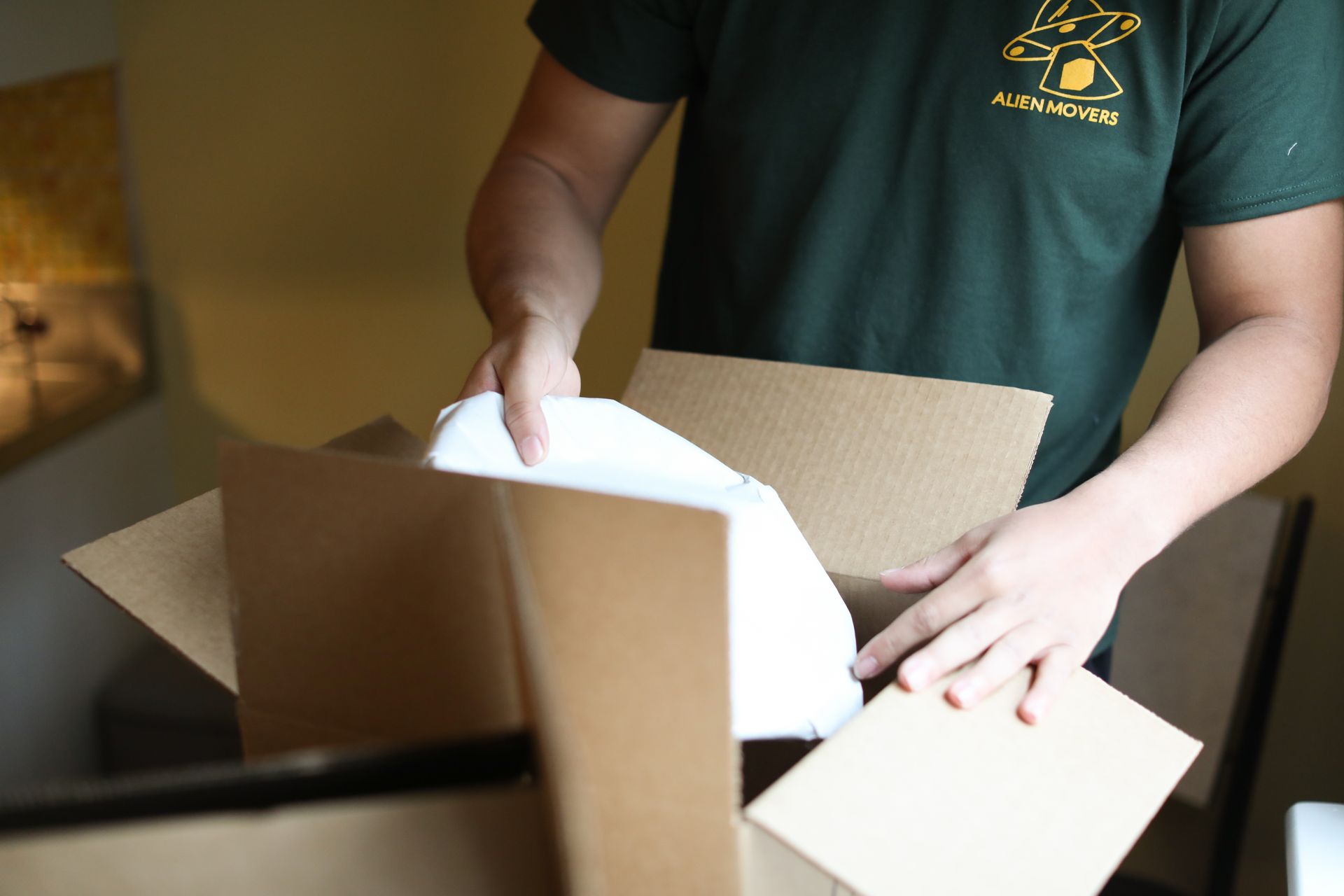 An Alien Movers staff member in a yellow shirt expertly packs kitchen items, ensuring safe relocation for Philadelphia moving services.