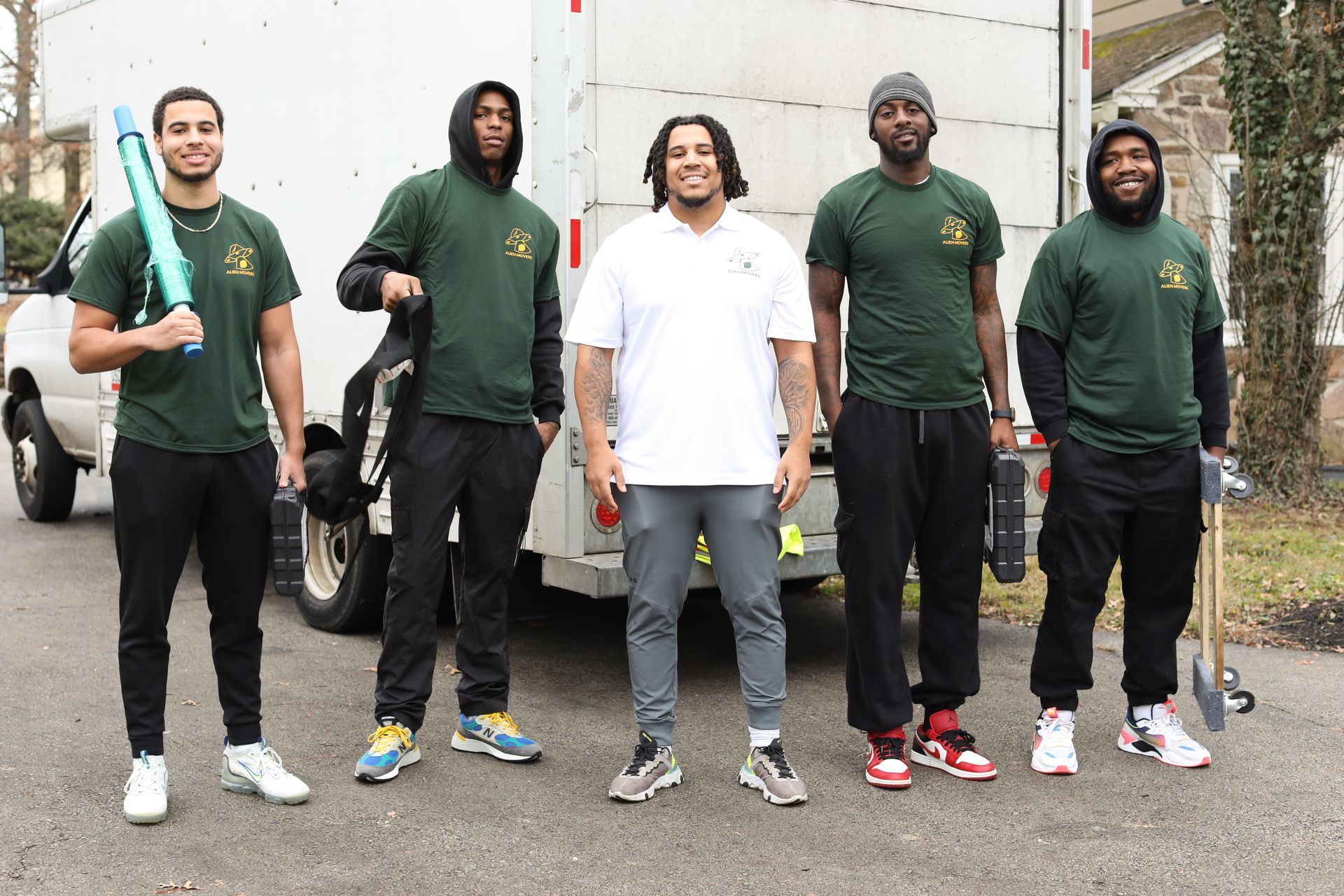 A team of five professional movers from Alien Mover, dressed in branded green uniforms, standing confidently in front of their moving truck, ready to provide top-notch Philadelphia Moving Services.
